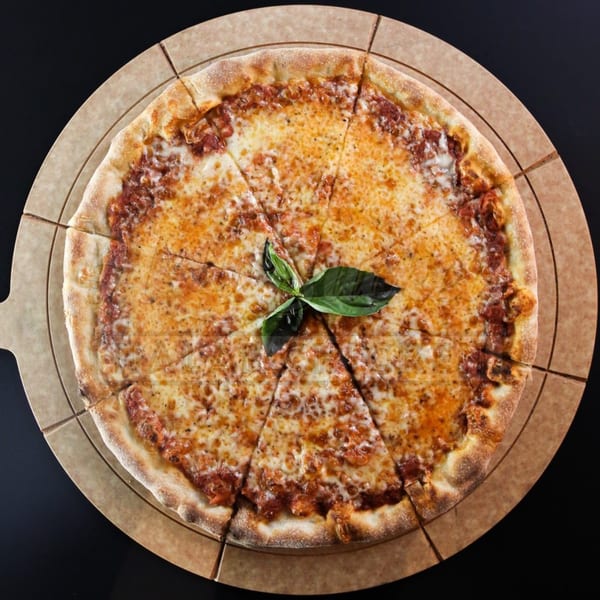 A whole Holy Buckets Halal Chicken & Chicken pizza, sliced, with basil garnish on a pizza stone.