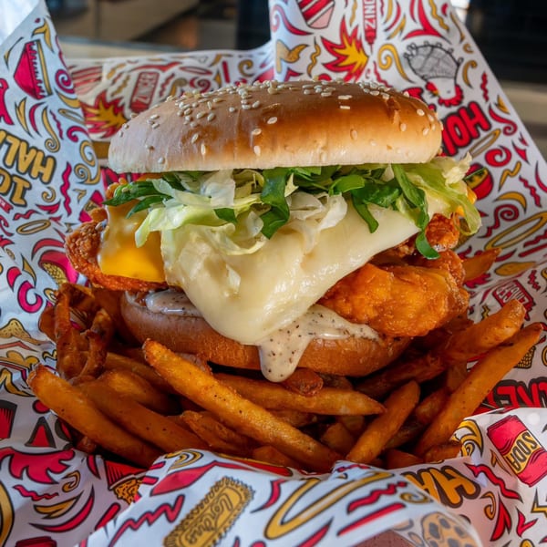 Holy Buckets Halal Chicken sandwich with melted cheese, lettuce, and sauce, served with fries.