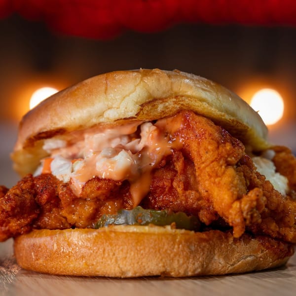Holy Buckets Halal Chicken sandwich with fried chicken, coleslaw, sauce, and pickles on a bun.