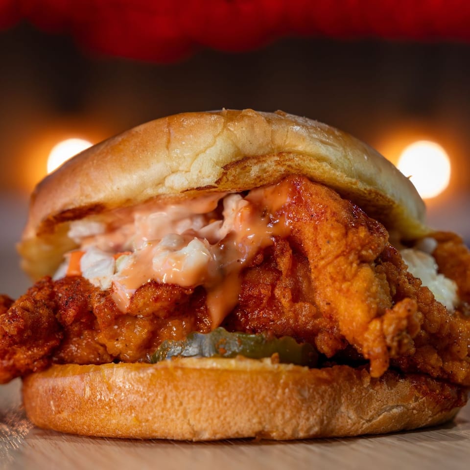 Holy Buckets Halal Chicken sandwich with fried chicken, coleslaw, sauce, and pickles on a bun.