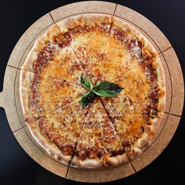 A Holy Buckets Halal Chicken & Chicken pizza, cut into slices, with basil on a round board.