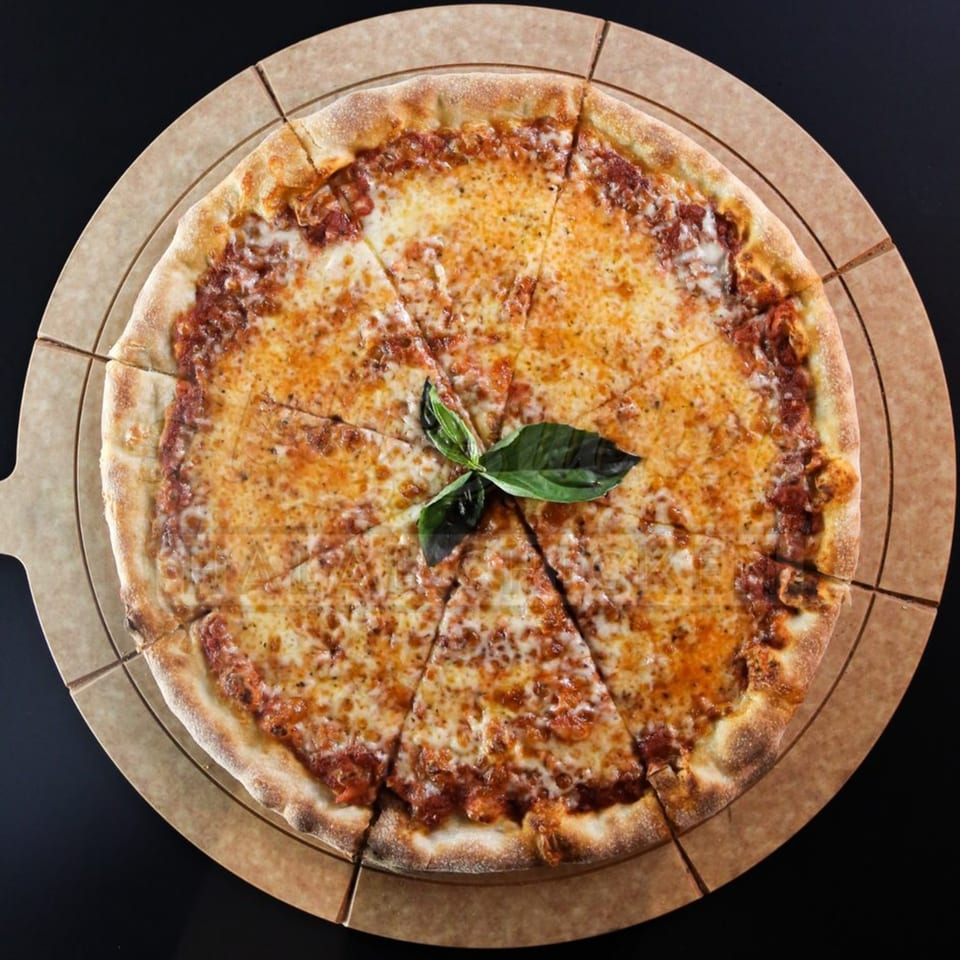 A Holy Buckets Halal Chicken & Chicken pizza, cut into slices, with basil on a round board.